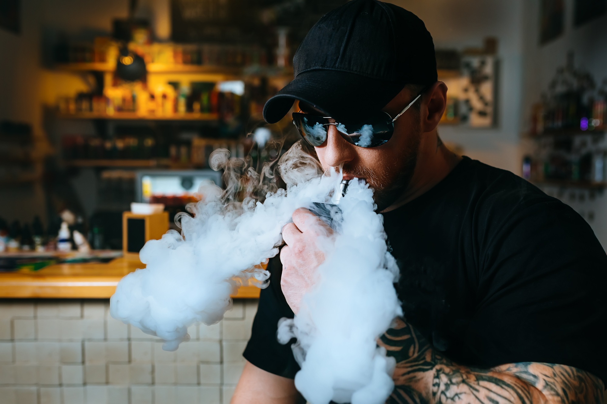 Brutal bearded man in sunglasses smoke an electronic cigarette and releases clouds of vapor at the